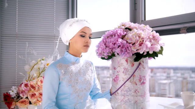 Hermosa-novia-musulmana-con-conforman-en-vestido-tradicional-azul-de-nikah-sentado-cerca-de-la-ventana