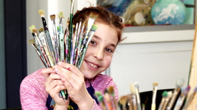 Cute-happy-girl-smiling-to-the-camera-holding-bunch-of-paintbrushes