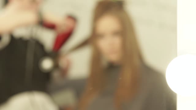 Verschwommene-Reflexion-im-Spiegel-Friseur,-Frau-Frisuren-lange-Haare-mit-Trockner-und-Pinsel-in-Beauty-Salon.-Hairstyling-Mode-Modell-in-Umkleidekabine