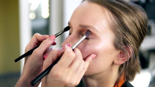 The-professional-make-up-artist-does-make-up-for-the-young-cute-model.-Artist-putting-an-eyes-shadows-using-two-brushes-and-does-it-together.-Close-up