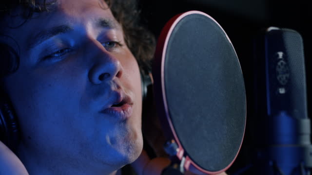 Young-handsome-singer-man-emotionally-writing-song-in-the-studio.-Recording-new-melody-or-album.-Male-vocal-artist-with-curly-hair-singing-alone.-Slow-motion.-4k