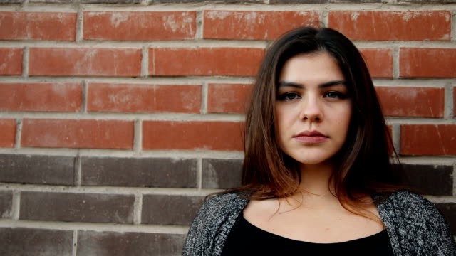 Portrait-of-a-young-serious-woman-against-a-brick-wall.-Slow-motion-shot.