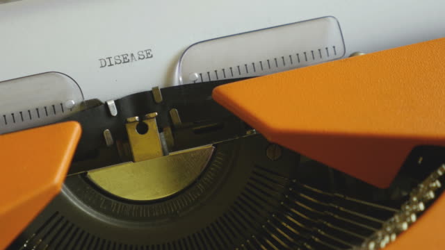 High-and-side-angle-footage-of-a-person-writing-DISEASE-on-an-old-typewriter,-with-sound