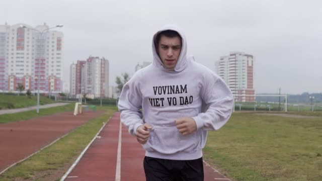 Young-man-training-at-stadium-in-morning.-Boxer-running-in-hoodie-outdoors