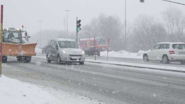 Zeitlupe:-Traktor-mit-Schnee-Pflug-und-Autos-fahren-auf-der-verschneiten-Straße.
