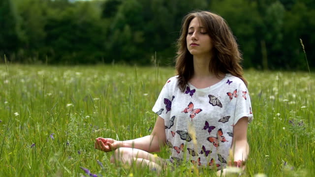 Female-meditating-outdoors-on-green-grass-in-summer,-sitting-lotus-concentration