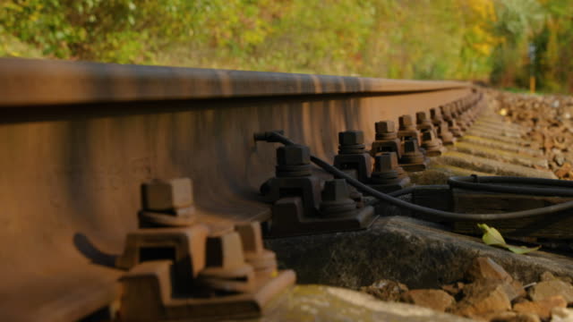A-close-up-view-of-the-large-screws-securing-the-train-tracks-during-a-sunny-day-while-slowly-passing-forward-looking-from-the-bottom-of-the-stones.