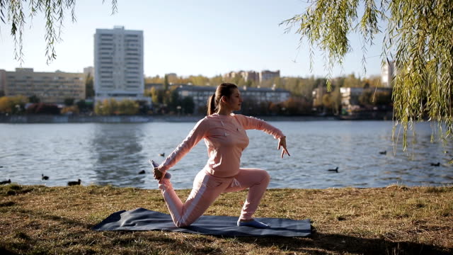 Schönes-Mädchen-in-einen-Trainingsanzug-auf-der-Stadt-am-Wasser-macht-Yoga.
