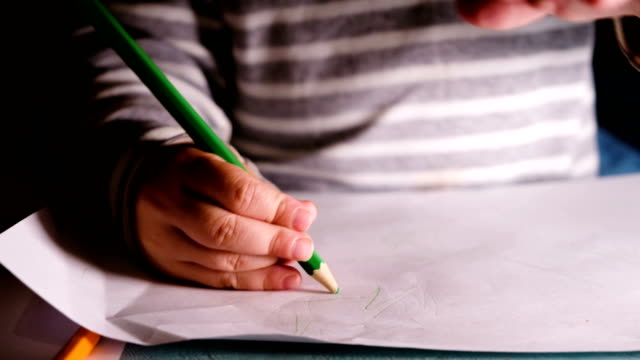 Small-child-draws-green-pencil-on-a-sheet-of-paper-close-up
