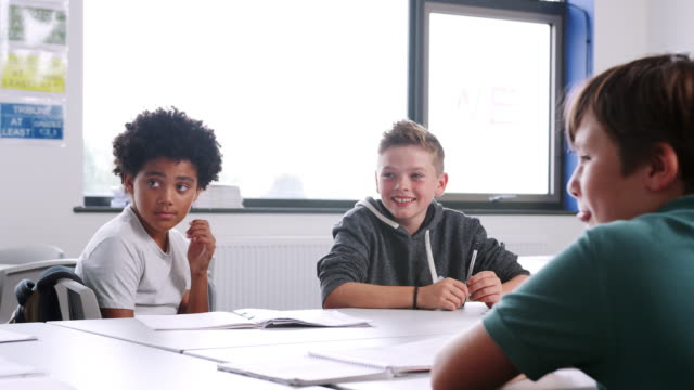 Drei-männliche-Gymnasiasten-an-Tisch-im-Klassenzimmer-sitzen-und-während-der-Lektion