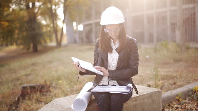 Studentin-in-einem-Helm-und-Schutzbrille-auf-der-Baustelle-untersucht-die-technische-Dokumentation