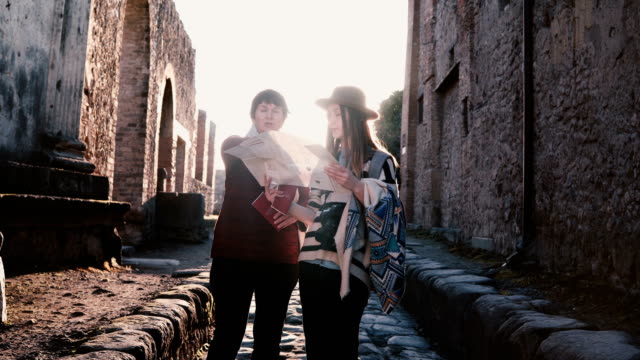 Happy-European-mother-and-daughter-with-a-map-exploring-historic-antique-streets-of-Pompeii,-Italy-on-a-vacation.