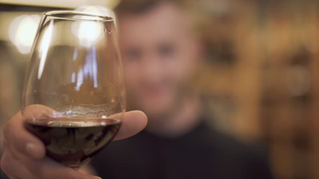 Closeup-of-a-wine-glass-that-holds-a-handsome-guy.-The-focus-moves-from-the-wine-glass-to-the-attractive-bearded-guy.-Wine-flows-down-the-edges-of-the-wine-glass.