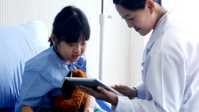 Doctor-visiting-Little-Girl-in-the-Hospital,-Little-Girl-looking-to-tablet-with-doctor-together-in-hospital.-People-with-Technology,-Healthcare-and-Medical-Concept.