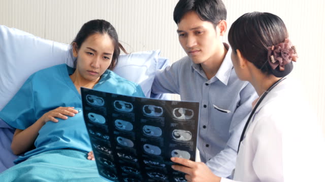 Doctor-showing-x-ray-film-to-pregnant-woman-and-her-husband-with-serious-emotion.-People-with-healthcare-and-medical-concept.