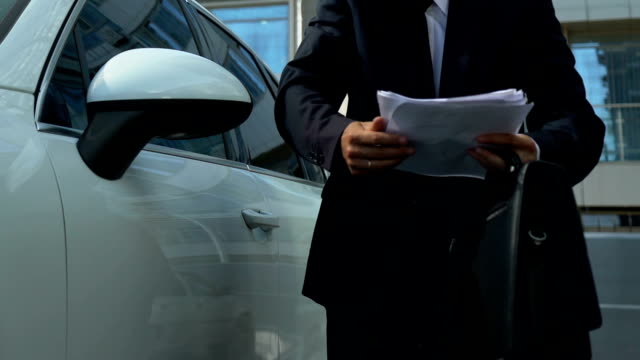 Male-boss-solving-business-issues-on-smartphone-near-vehicle,-holding-documents