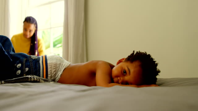 Padre-negro-ayudando-a-su-hijo-a-cambiar-su-ropa-en-la-cama-en-una-casa-confortable-4k
