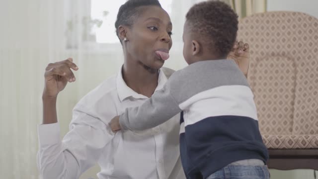 Fröhliche-afroamerikanische-Mutter-spielt-mit-ihrem-frechen-Kind.