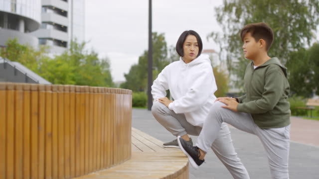 Asian-Mother-and-Son-Stretching-Legs-during-Outdoor-Workout