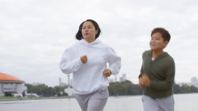 Sportliche-asiatische-Mutter-und-Sohn-Joggen-im-Freien-entlang-Urban-Riverside
