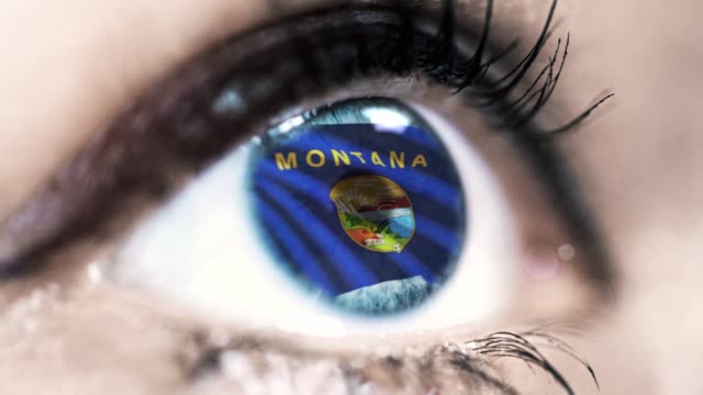 Mujer-ojo-azul-en-primer-plano-con-la-bandera-del-estado-de-Montana-en-iris,-estados-unidos-de-América-con-movimiento-de-viento.-concepto-de-vídeo