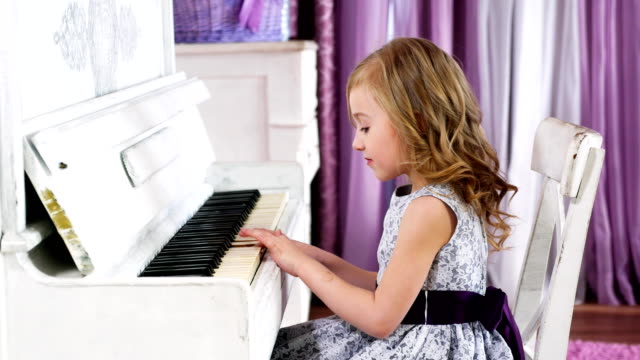 niña-rubia-juega-piano,-muchacha-en-un-vestido-con-un-cinturón-púrpura,-de-4k