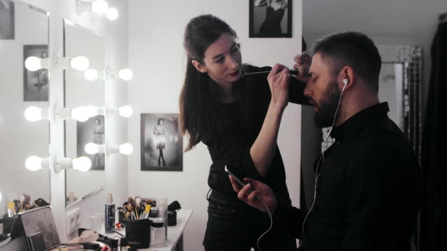Makeup-stylist-applying-makeup-on-face-bearded-man-in-dressing-room