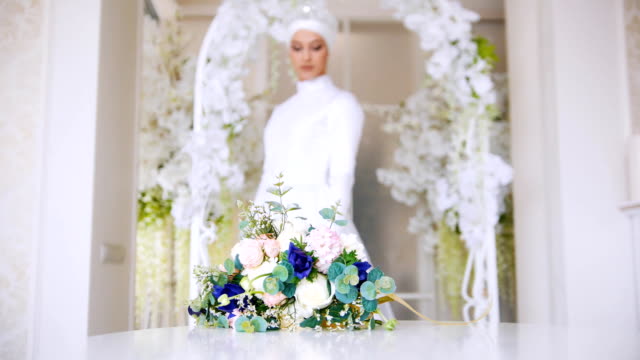 Schöne-Braut-im-weißen-traditionellen-muslimischen-Kleid-mit-Blumenstrauß