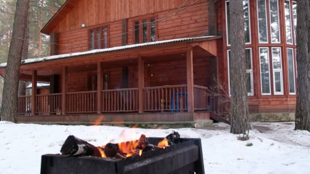Panoramic-video-of-open-fire-in-iron-brasier-barbecue-with-cottage-on-background