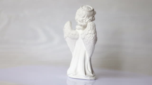 white-angel-statue-revolves-on-a-stand-against-a-white-wooden-wall.-FullHD-format-video