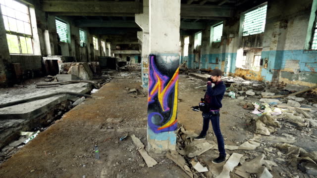 High-angle-shot-of-young-urban-artist-decorating-high-column-in-old-damaged-building-with-abstract-image.-Modern-art,-street-painter,-creativity-and-people-concept.