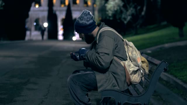 Homeless-walking-in-the-city-park-at-night-,countings-his-alms