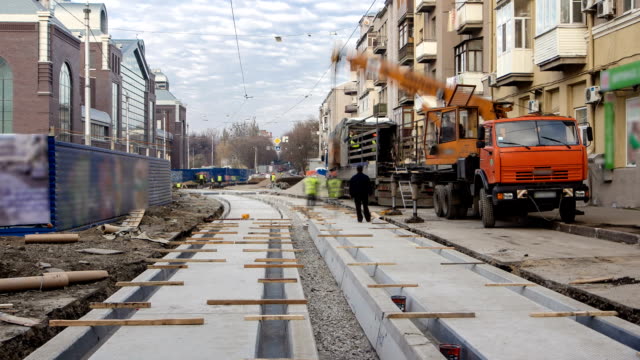 Tram-rails-at-the-stage-of-their-unloading-from-truck-by-crane-on-concrete-plates-on-the-road-timelapse
