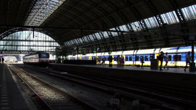 Silueta-de-pasajeros-a-pie-en-la-plataforma-a-bordo-de-un-tren-en-la-estación-Central-de-Amsterdam-en-Europa.