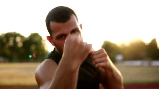 Portrait-of-strong-young-man-in-sport-shorts-and-T-shirts-boxing-and-punching-invisible-opponent-while-training-outdoors,-slow-motion