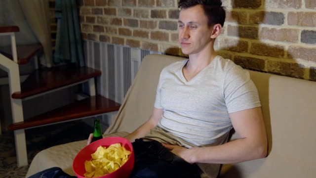 Young-man-with-beer-and-chips-in-front-of-TV