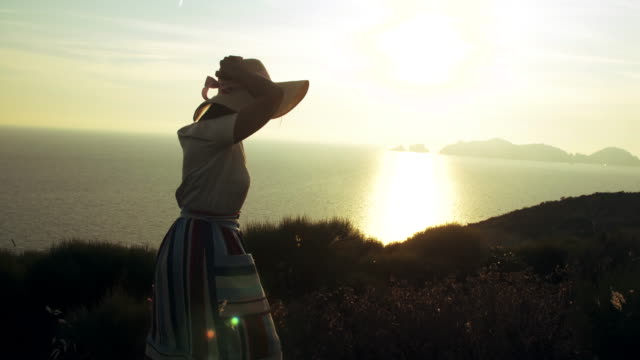 Schöne-junge-Frau-bunte-Kleid-Mode-mit-Rock-und-Hut-tragen-Blumen-im-Korb-bei-Sonnenuntergang-auf-der-Insel-Ponza-Berg-Italien.