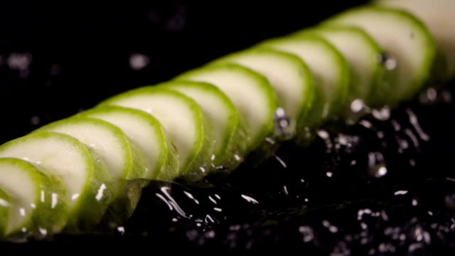 In-Scheiben-geschnittene-Zucchini-fallen-in-den-nassen-Tisch.-Zeitlupe-480-fps