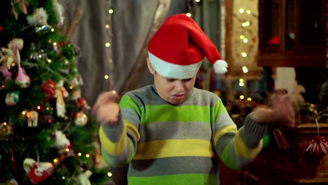 The-boy-in-the-sweater-and-the-hat-of-Santa-Claus-is-upset-and-offended.-He-has-no-gift.-Against-the-background-of-Christmas-lights