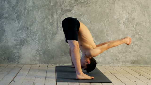 Sporty-muscular-young-yogi-man-doing-Wide-Legged-Forward-Bend,-Prasarita-Padottanasana-posture-(Dandayamana-Bibhaktapada-Paschimotthanasana