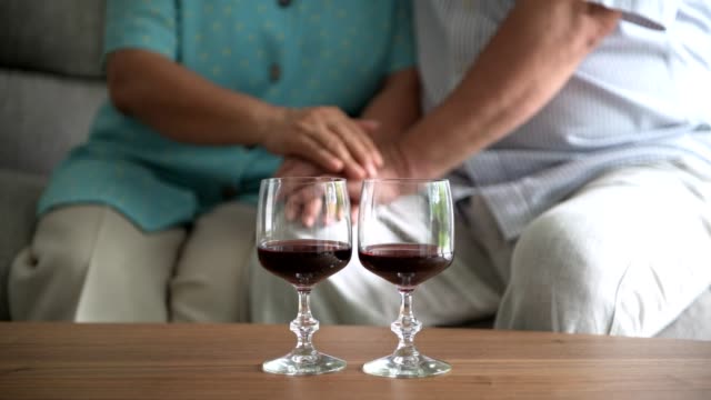 Senior-couple-sitting-and-talking-with-red-wine-glass-on-table-in-living-room.
