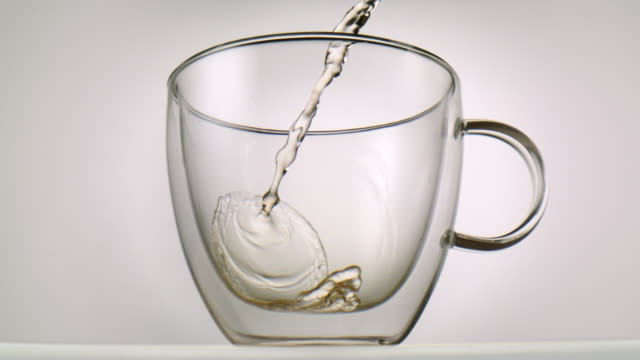 Hot-tea-being-poured-inside-a-glass-in-front-of-white-background-in-slowmotion