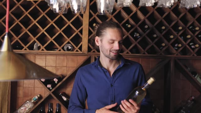 Lächelnder-Mann-mit-Flasche-Wein-im-Keller-im-Weingut-Restaurant