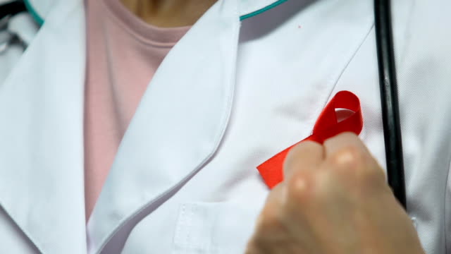 Doctor-pins-up-red-ribbon,-concept-of-AIDS-awareness,-prevention-and-treatment