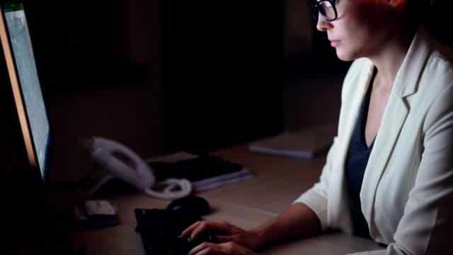 Zuversichtlich-Mädchen-in-formelle-Kleidung-Büroangestellter-nutzt-Computer-spät-in-die-Nacht-arbeiten-allein-im-dunklen-Büro-am-Schreibtisch-sitzen-und-mit-Blick-auf-den-Bildschirm.-Job-und-Millennials-Konzept.