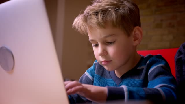 Close-up-profile-shoot-of-small-boy-playing-games-on-laptop-and-his-mother-observing-his-activity-sitting-nearby.