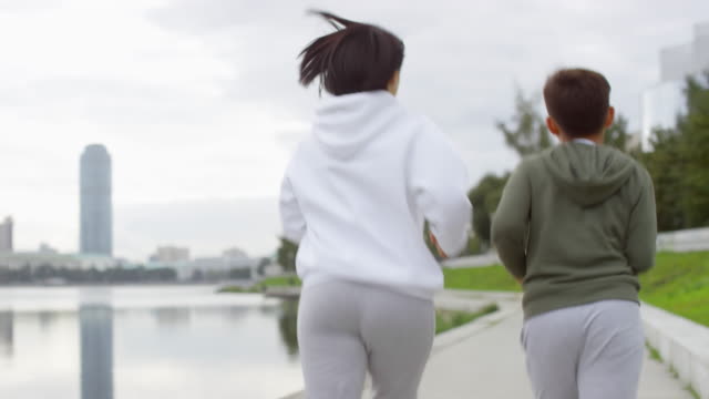 Back-View-of-Mother-and-Son-Jogging-along-Riverside-in-City