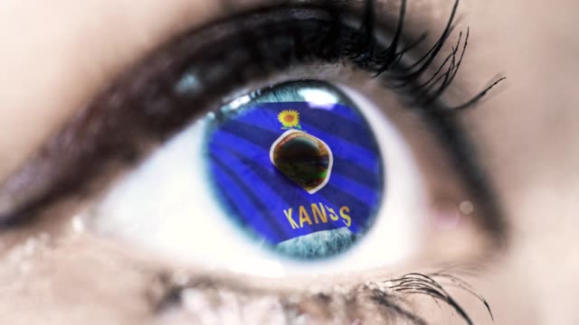 Woman-blue-eye-in-close-up-with-the-flag-of-Kansas-state-in-iris,-united-states-of-america-with-wind-motion.-video-concept