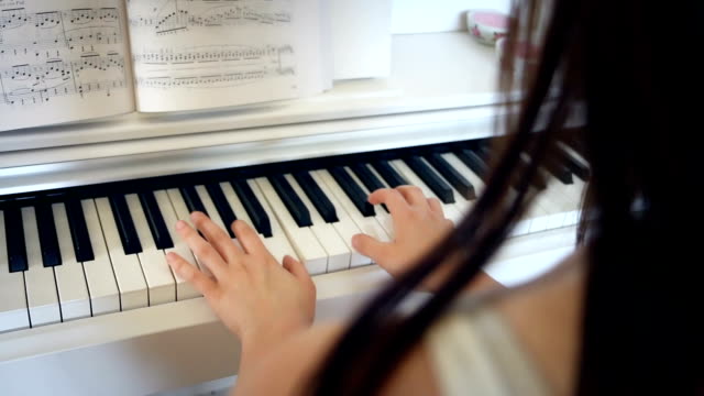 Young-brunette-woman-is-playing-piano-in-bright-room,-hand-held