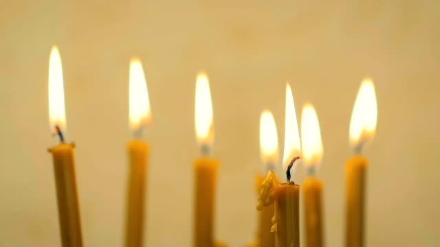 SLOW-MOTION:-close-up-of-a-lot-of-beautiful-wax-candles-burning.-Yellow-background.